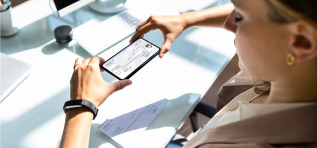 Photo of a woman using her cellphone to take a photo of a check.