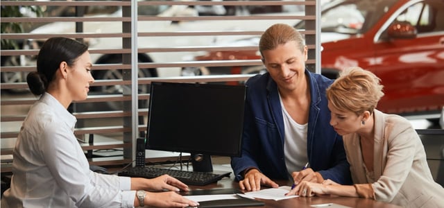 Photo of a couple going over paperwork at a car dealership.