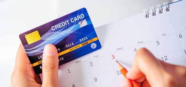 One hand hold a Credit card while other holds orange pencil pointing the date on calendar for checking and planning of billing due date One hand hold a Credit card while other holds orange pencil pointing the date on calendar for checking and planning of billing due date