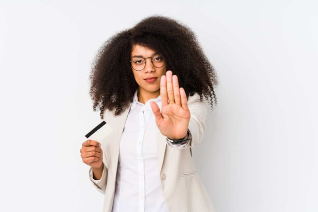 Young business woman holding a credit card standing with outstretched hand showing stop sign, preventing you.