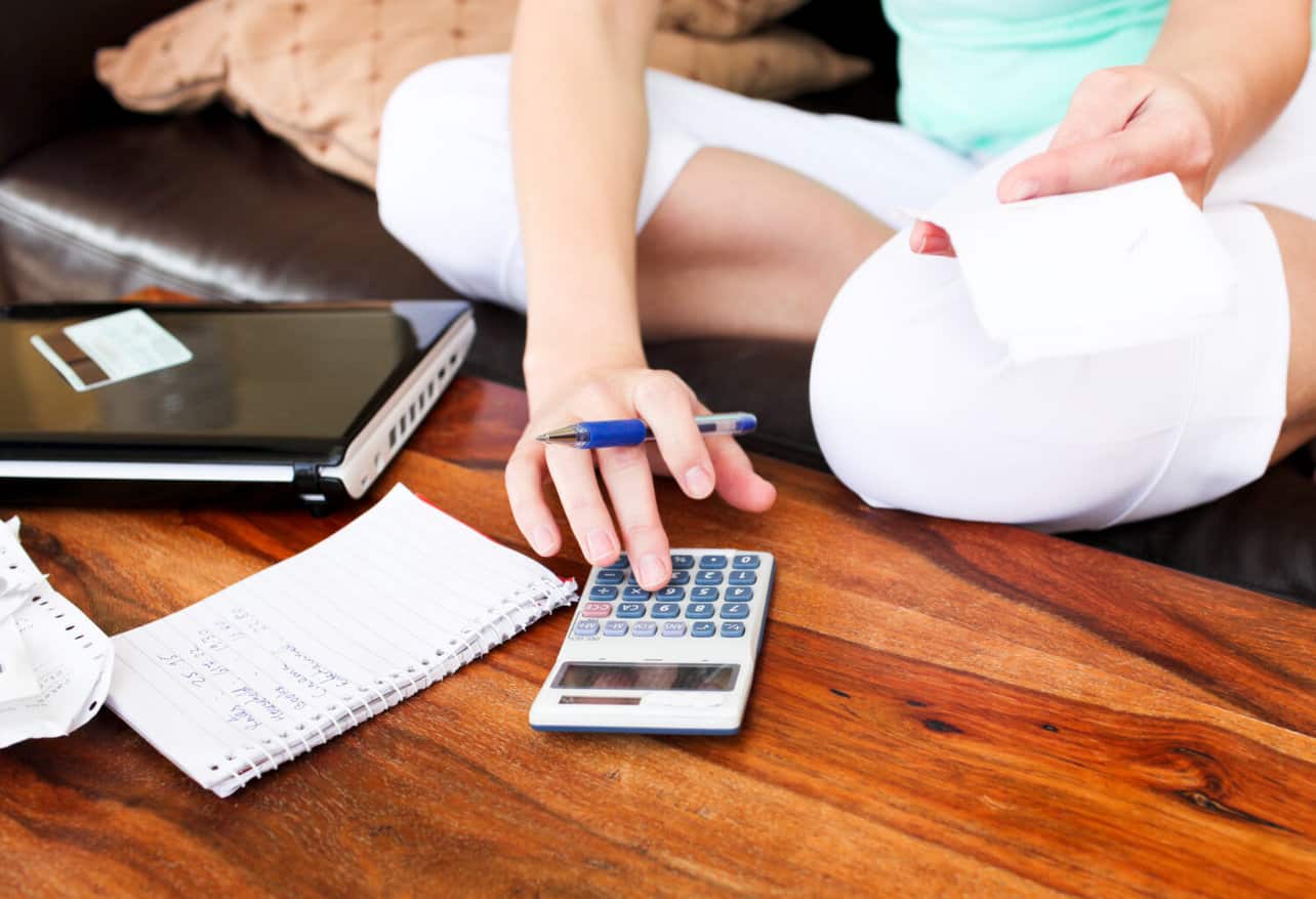 Woman using a calculator sitting on the couch, calculating credit card debt concept