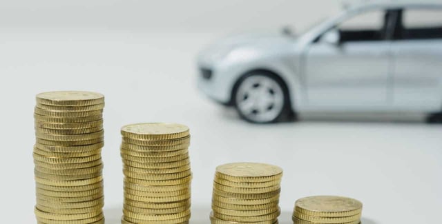 Lower interest rates. Stacked coins in front, a car is out of focus in the back.