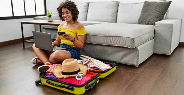 Woman sitting on the floor next to a suitcase looking at a credit card.