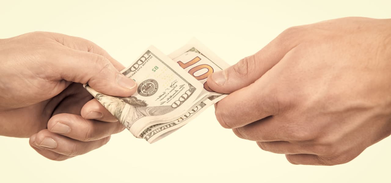 Two hands exchanging $100 bills