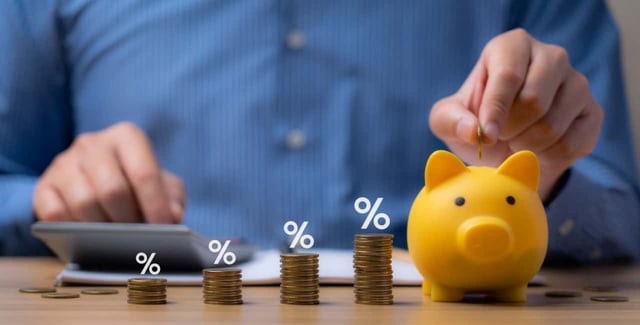 Yellow piggy bank next to a calculator and a stack of coins increasing in height with percentage symbols above each