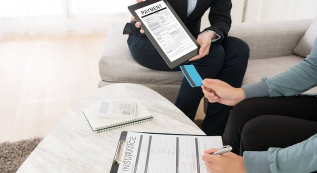 woman buying insurance sitting on living room sofa signing contract and using personal credit card