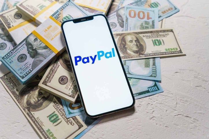 PayPal logo on phone on top of money PayPal logo on phone on top of money